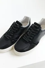 Zapatillas urbanas de cuero negro con cordones negros y suela blanca.