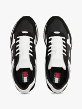 Zapatillas de estilo running con silueta de corte bajo, cordones y paneles en texturas mixtas. Combinan materiales negros, blancos y grises, destacando el parche con el logo de Tommy Jeans en el lateral.