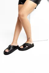 Sandalias bajas de cuero color blanco con suela negra y hebilla metálica.