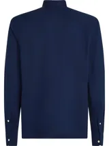 Camisa azul marino de corte slim, confeccionada en tejido dobby de algodón con Flex Technology, cuello abotonado, puños redondeados con dos botones y logo de Tommy Hilfiger bordado en el pecho.