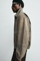 Cazadora de hombre color verde oliva, confeccionada en piel con acabado ante. Presenta un corte boxy fit, cuello solapa, cierre frontal de cremallera, bolsillos delanteros y elásticos en puños y bajo.