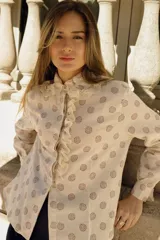 Camisa color crema con estampado de círculos marrones, cuello con volados y puntilla, y cierre frontal con botones y volados.