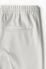 Pantalón de vestir gris claro, de corte slim fit, con cintura elástica y cordón ajustable. Presenta bolsillos laterales y traseros ribeteados, pliegues cosidos y doblez en el bajo.