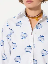 Camisa blanca de poplin con lycra y estampado de hongos en azul. Tiene ojales color bordó en la cartera y puños, y costura de refuerzo en forma de X en el puño.