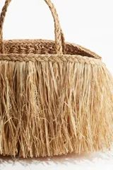 Bolso de mano tipo shopper confeccionado en paja de papel color natural con efecto desflecado. Tiene dos asas trenzadas y no está forrado.