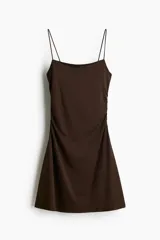 Vestido corto marrón de breteles finos, escote cuadrado, corte ajustado y falda con leve vuelo. Presenta frunces laterales que generan un efecto drapeado.