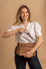 Bandolera de diseño moderno, color beige rosado, con correa regulable y bolsillo frontal con cierre.