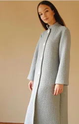 Bata gris claro con textura capitoné, cuello mao, corte recto, abotonada al frente y con bolsillos laterales.