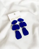 Par de aros colgantes con tres piezas geométricas de acrílico color azul eléctrico, unidas por argollas doradas.