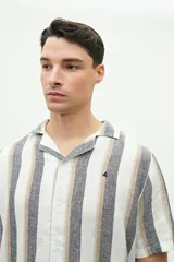 Camisa de manga corta confeccionada en lino y algodón a rayas verticales en tonos blanco, gris y beige. Tiene cuello tipo cubano, corte regular y logo bordado en el pecho.