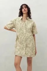 Vestido camisero corto color verde claro con estampado de hojas en blanco. Tiene cuello camisero, cierre frontal con botones y corte recto.