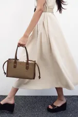 Bolso tipo shopper color marrón con doble asa corta y correa larga extraíble. Tiene detalle de pespuntes y anilla metálica decorativa. Incluye bolsa de tela interior extraíble con cierre fruncido.
