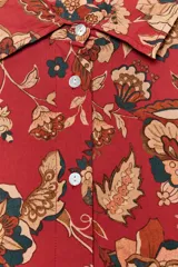 Camisa larga de algodón con estampado floral en tonos rojos, marrones y verdes. Tiene cuello solapa, manga larga con puños y bajo redondeado.