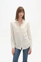 Camisa de viscosa color crema con finas rayas verticales negras, corte al cuerpo, cuello camisa y dos bolsillos frontales con tapa. Posee botones frontales y mangas largas con puño.