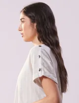 Blusa de lino color blanco con rayas verticales, de la marca Cable & Gauge. Tiene hombros con aplique de botones.