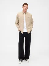 Camisa de manga larga color beige, de corte clásico, con cuello abotonado, bolsillo en el pecho y logo de oso bordado.