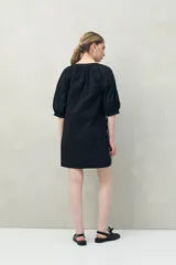 Vestido corto blanco de algodón con bordado floral en relieve, escote redondo con abotonadura frontal y mangas amplias.