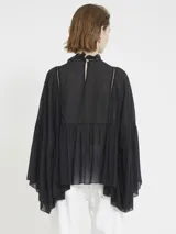 Blusa negra de gasa liviana, con silueta holgada y mangas amplias. Tiene volados frontales, detalles de encaje y cuello alto fruncido, con un estilo romántico y bohemio.