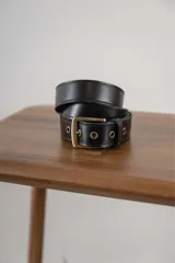 Cinturón negro de cuero con hebilla metálica dorada y ojales metálicos.