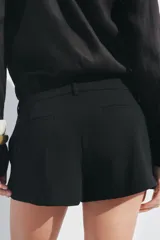 Shorts negros de tiro medio con cintura con trabillas y pliegues delanteros. Cierre frontal con cremallera, botón y ganchos metálicos.