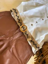 Cinturón de yute color beige con bordado de hilo negro en forma de zigzag y hebilla circular de madera.