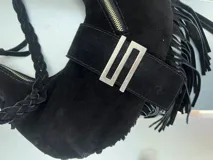 Cartera negra tipo hobo de gamuza con flecos, cierre superior con cremallera y asa de hombro trenzada.