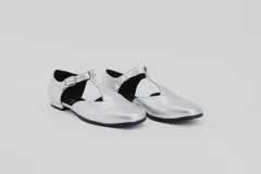 Zapato flat de cuero con estampado de vaca en blanco y negro, con tira delantera y hebilla lateral.