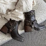 Bota corta de cuero color marrón oscuro, con caña media, punta cuadrada y taco de madera. Presenta correas de cuero con hebillas metálicas y estribo desmontable.