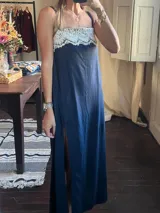 Vestido largo azul marino con escote recto adornado con una banda de encaje blanco. Tiene tirantes finos y una abertura lateral pronunciada en la falda.