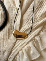 Collar con dije irregular dorado y tiento negro.