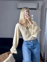 Blusa blanca de mangas largas con volados en los puños y escote con lazo.