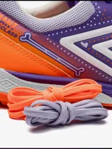 Championes de fútbol Umbro, color violeta con detalles en naranja y blanco. Presentan un diseño texturizado en la parte delantera y el logo de Umbro en los laterales. La suela es de color naranja con tapones para césped sintético.
