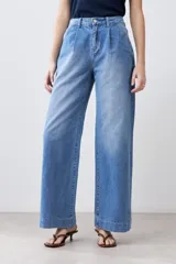 Pantalón de jean celeste de corte ancho, con cintura alta, pinzas y bolsillos laterales. Se ajusta a la cintura con un cinturón de cuero marrón.