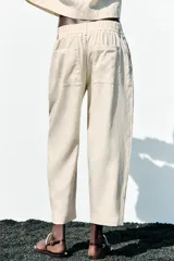Pantalón color crema de tiro alto con pinzas delanteras y cintura elástica en la espalda. Tiene bolsillos delanteros y traseros.