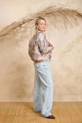 Bomber estampada con motivos florales y de aves en tonos pastel, con cuello mao, cierre frontal con botones dorados, bolsillos laterales con solapa y puños elásticos.