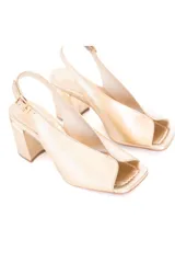 Zapato de cuero color dorado, con taco cuadrado y punta abierta. Presenta una tira fina con hebilla al tobillo.