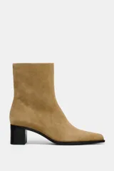 Botín de mujer de caña media color beige, confeccionado en serraje con detalle de pespuntes en la parte delantera. Tiene tacón bloque medio y cierre mediante cremallera lateral.