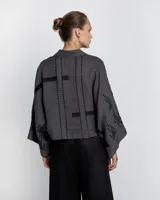 Camisa gris con bordados negros, de corte holgado y mangas anchas.