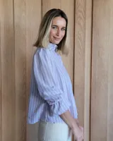 Blusa color beige con cuello con volados, mangas largas abullonadas con puños elásticos y cierre con botones en la parte delantera.