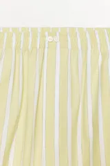 Pantalón tipo pijamero con tiro alto y cintura elástica, confeccionado en hilatura con algodón y lino. Presenta un estampado a rayas verticales en color amarillo y blanco, y detalle de botones decorativos en el delantero.