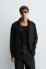 Camisa negra de manga larga con cuello italiano y cierre frontal de botonadura. Presenta un tejido con estructura de fácil cuidado.