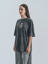 Remera negra con efecto nevado, corte oversize y estampado de Mickey Mouse sobre una patineta.