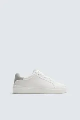 Zapatillas deportivas blancas con detalle en gris en el talón y suela con volumen.