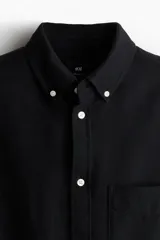 Camisa negra de algodón Oxford con cuello americano, tapeta clásica, bolsillo superior abierto y canesú en la espalda. Mangas largas con puños abotonados y bajo levemente redondeado. Corte estándar para una silueta clásica y cómoda.