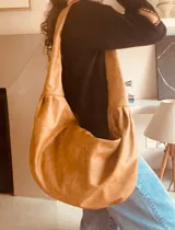 Bolso tipo hobo de cuero color camel, con correa ancha para el hombro y bolsillo interno con cierre.