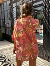Camisa oversize de manga corta con cuello solapa y botones frontales. Presenta un estampado floral grande en tonos rosados, naranjas y verdes.