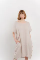 Vestido corto color beige confeccionado en lino, de corte recto y calce holgado. Presenta botones decorativos en los laterales y bolsillos laterales.