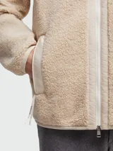 Buzo de tejido tipo teddy en color beige, con cierre frontal completo, cuello alto y un bolsillo de parche en el pecho con solapa y el logotipo de Moncler. Presenta bolsillos laterales con ribete y un diseño de corte holgado.
