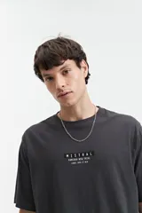 Remera gris oscuro de manga corta con cuello redondo y estampado frontal con el texto "MISTRAL KAMIOKA NEW TRIAL SINCE 1976 // NLD".
