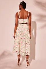 Vestido midi blanco con bordado de flores rojas y amarillas, tirantes finos, corte en la cintura y aberturas laterales.